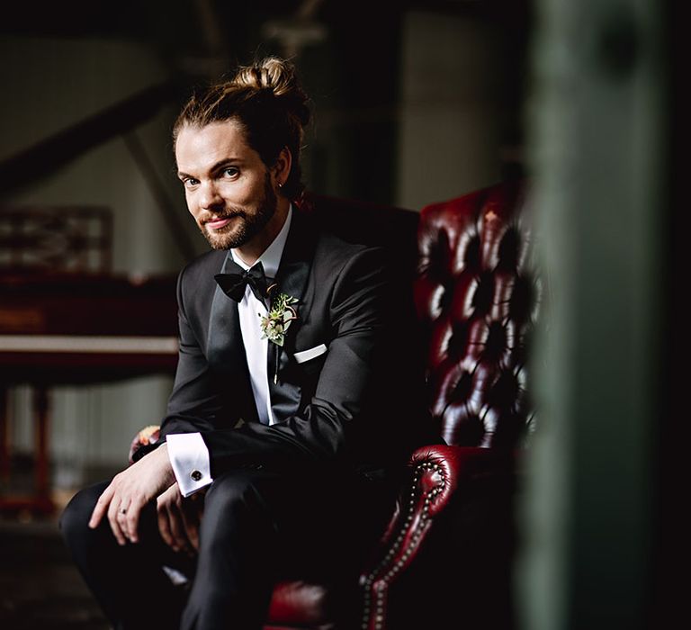 Groom wears his hair tied up with black-tie and floral buttonhole 