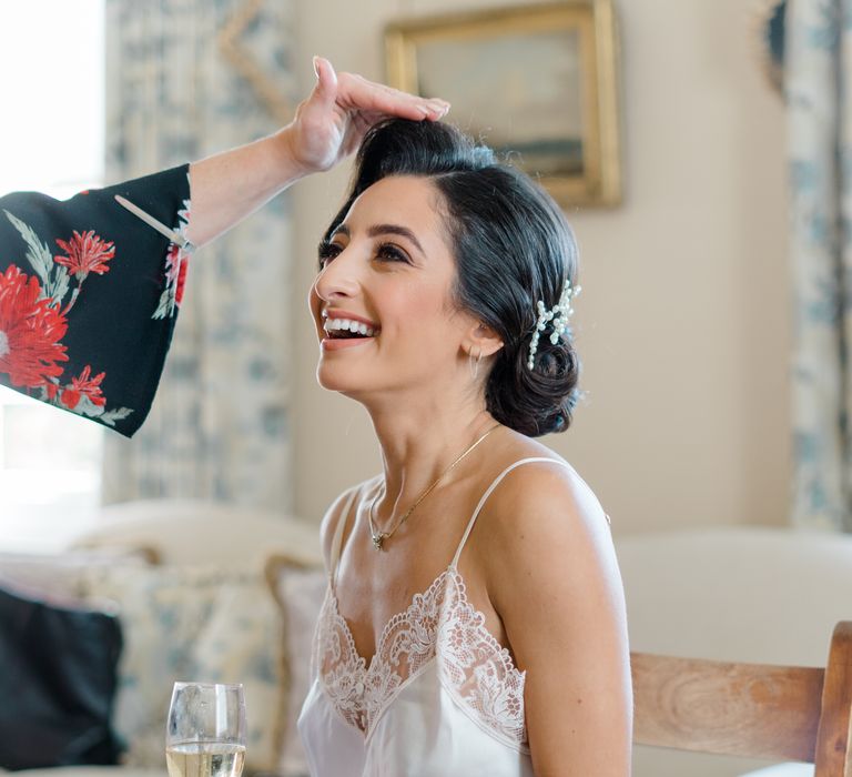 Bride wears her dark hair pinned back complete with pearl hair accessory and silk lace pyjamas 