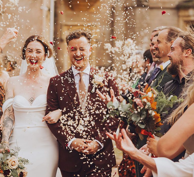 Bride in Vera Wang wedding dress and her groom walk through white confetti after wedding ceremony