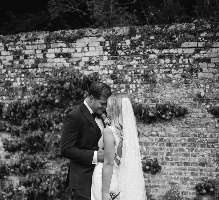 Groom in black tie rests his forehead against the bride who wears a plunging satin wedding dress