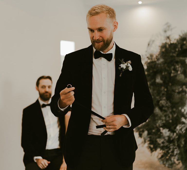 Groomsmen in black tie holding the groom's plain wedding band on a ribbon for the ring warming ceremony 