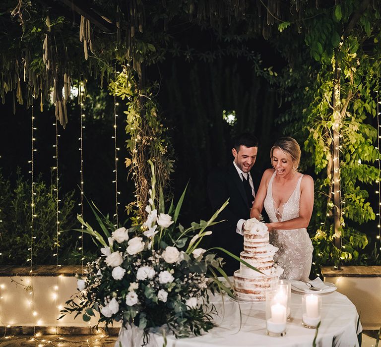 Bride in lace wedding dress & groom in black-tie cut three tier naked wedding cake