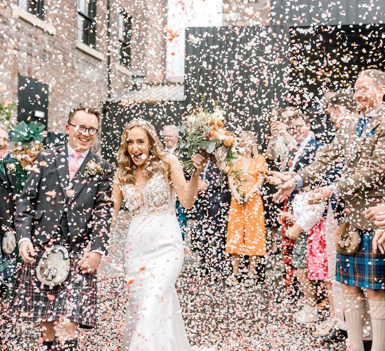 Bride & groom walk through colourful confetti exit after Christian wedding ceremony 