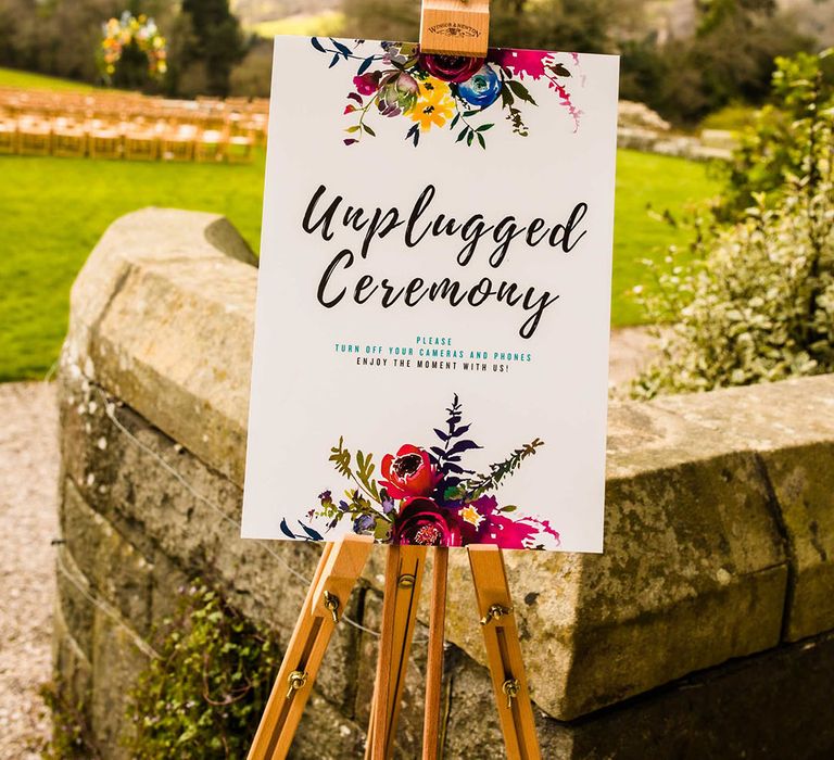 Unplugged wedding ceremony sign on wooden easel complete with colourful floral illustration 