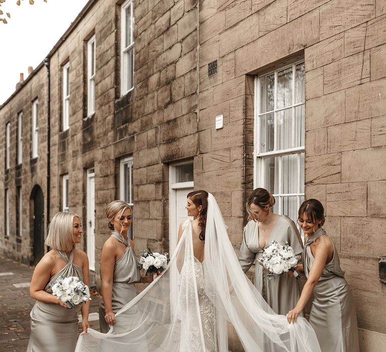 Bridesmaids in sage green satin bridesmaid dresses with white rose bouquets holding the bride's Watteau train wedding dress 