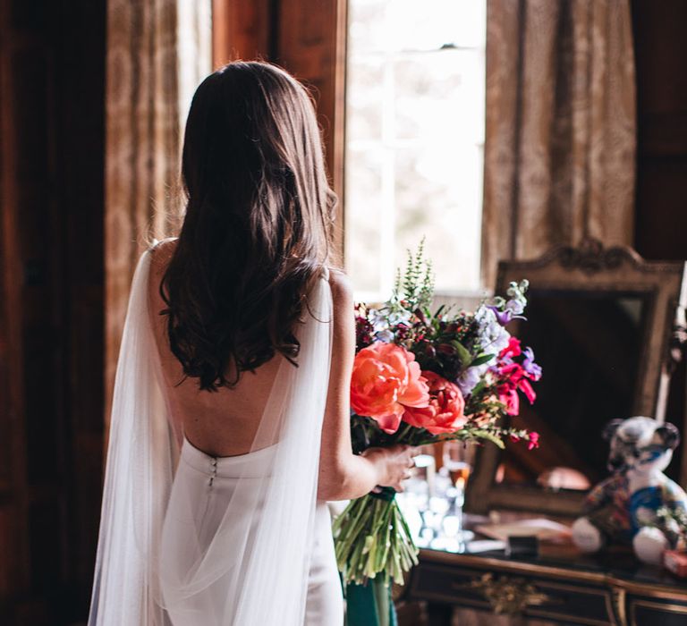 Bride in open back Kyha wedding dress with tulle wings holding a bright pink and red wedding bouquet 