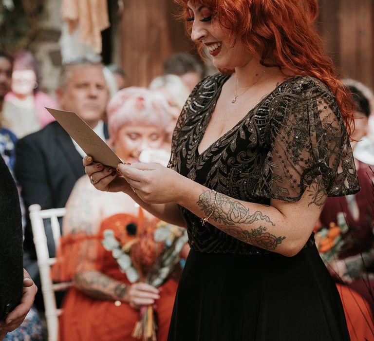 Bride in sparkly embellished v-neck black wedding dress doing wedding reading at Westcott Barton, Devon wedding venue 