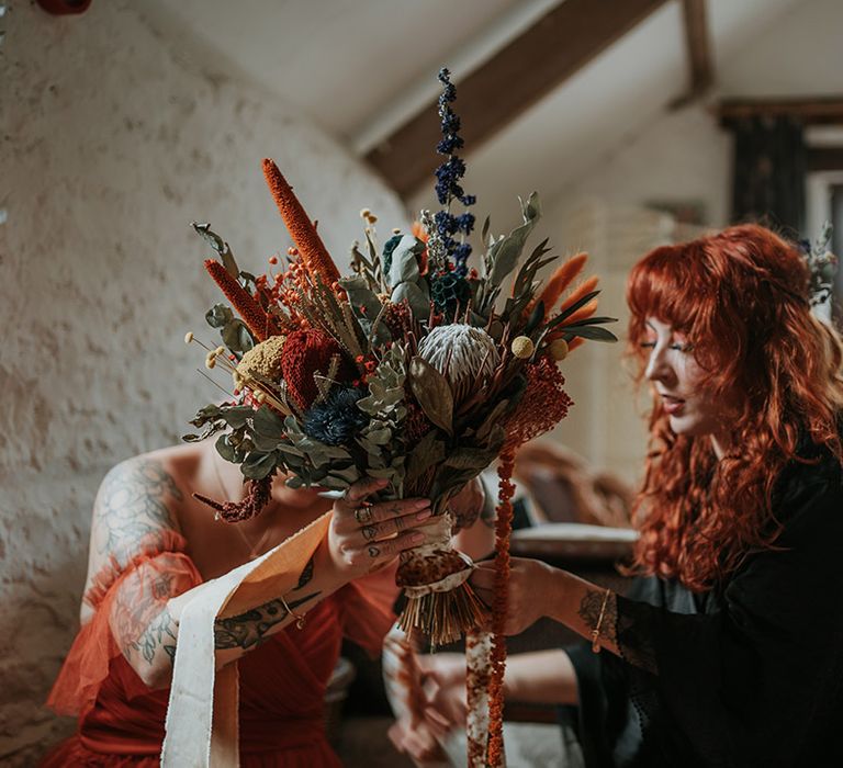 Bride in black wedding dress holding large yellow, blue and orange dried flower bouquet 