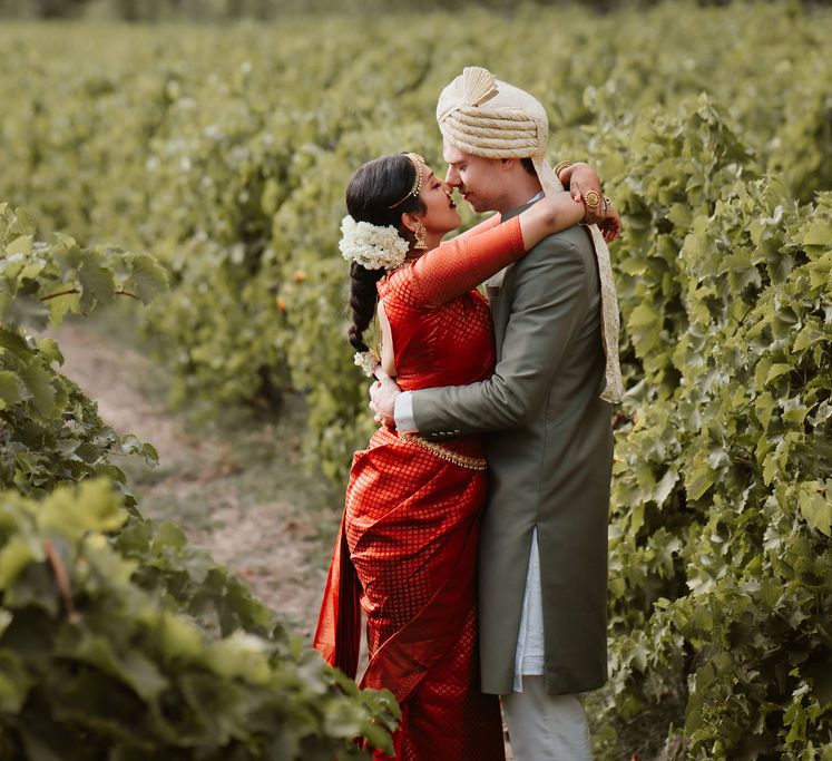 Groom in a green Sherwani and bride in a red Lehenga kissing in the vineyards at their destination wedding 