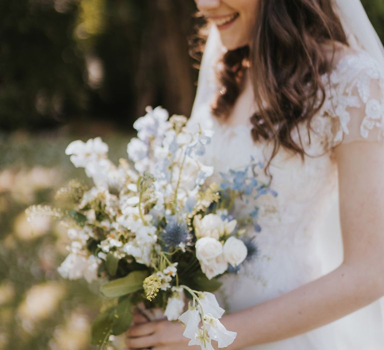 Blue and white wedding bouquet held by bride in short sleeve wedding dress and veil for rustic wedding at Badgers Holt in Dartmoor 