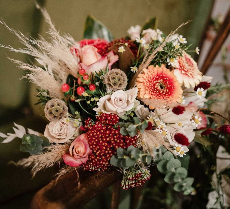 Foliage, garden rose, pampas grass and dried flower boho bouquet on crushed velvet olive green loveseat at The Barn at Avington 