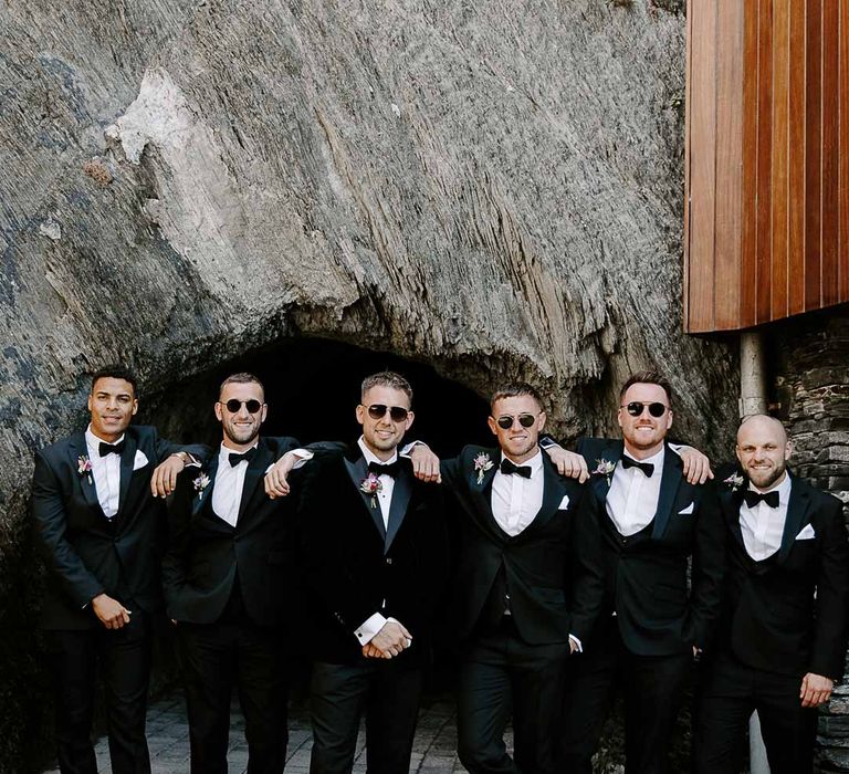 Grooms party wearing matching classic black-tie tuxedos, bow ties and grooms sunglasses 