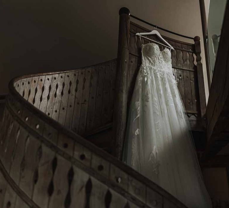 Sweetheart neckline lace wedding dress hanging on the spiral staircase at Lains Barn wedding venue 