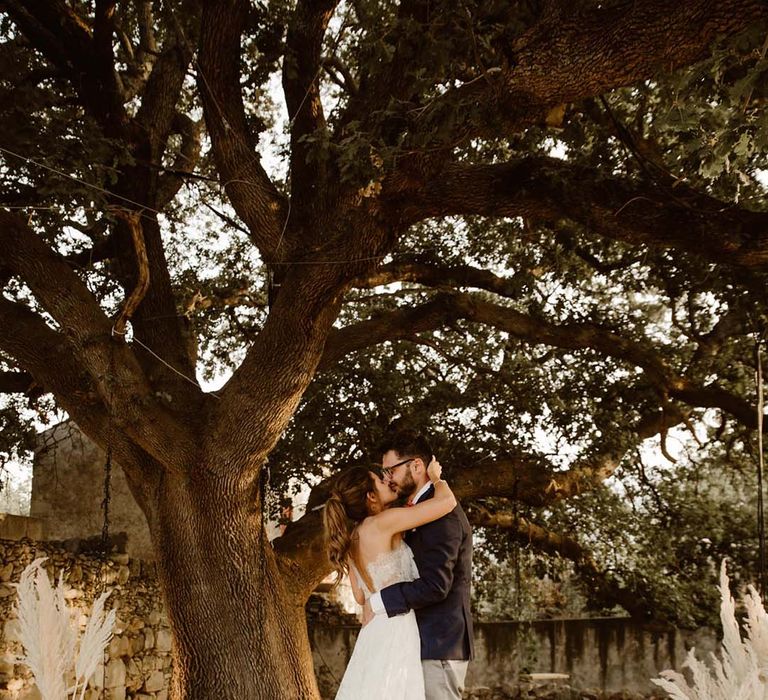 bride in a strapless lace wedding dress kissing her groom at outdoor ceremony with pampas grass and wool decor for greece destination wedding