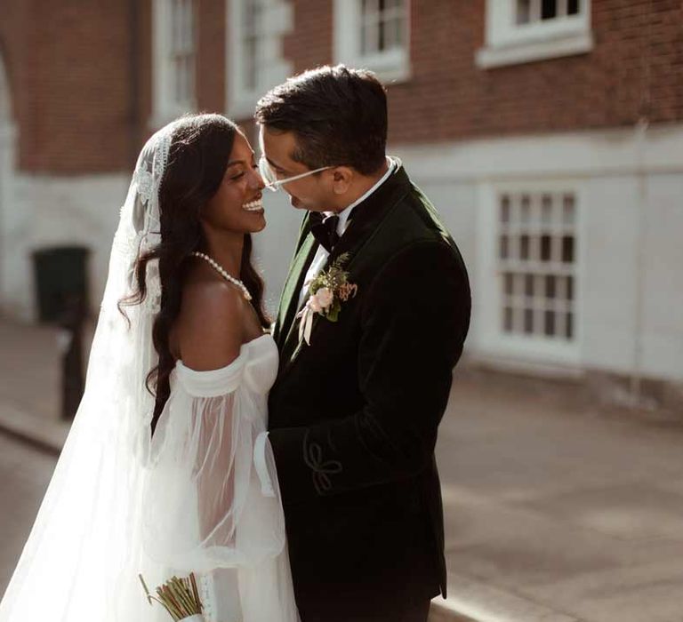 Groom in bottle green velvet grooms suit, black bowtie and chic boutonniere embracing bride in off the shoulder layered tulle wedding dress and floral embroidered cathedral-length veil at Inner Temple Hall vow renewal 