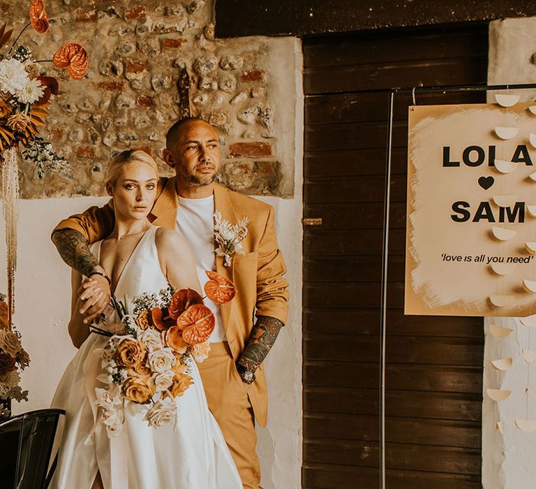 Groom in light orange wedding suit with the bride at their wedding with personalised wedding sign 