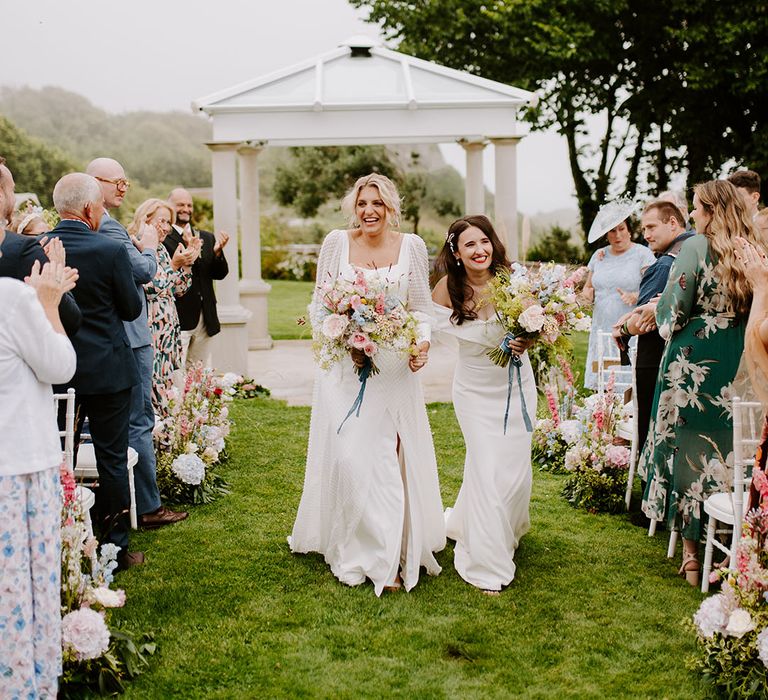 Two brides walking back down the aisle at outdoor wedding ceremony with pastel wedding bouquets 