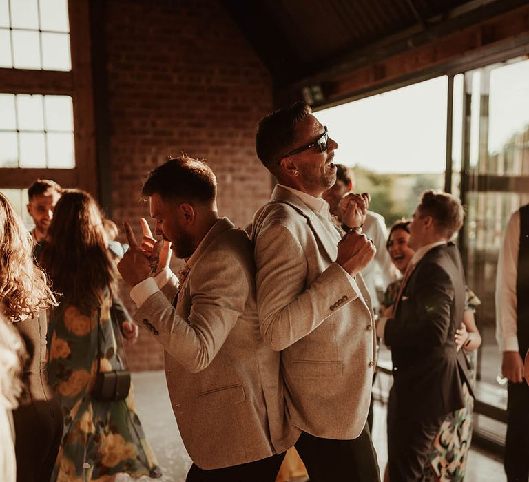 Groom and groomsmen in matching stone suits dancing together at The Giraffe Shed industrial wedding venue 