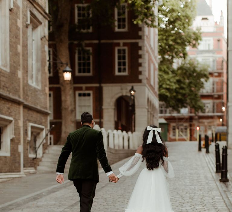 Bride and groom walking hand in hand with the bride wearing a white hair bow accessory 