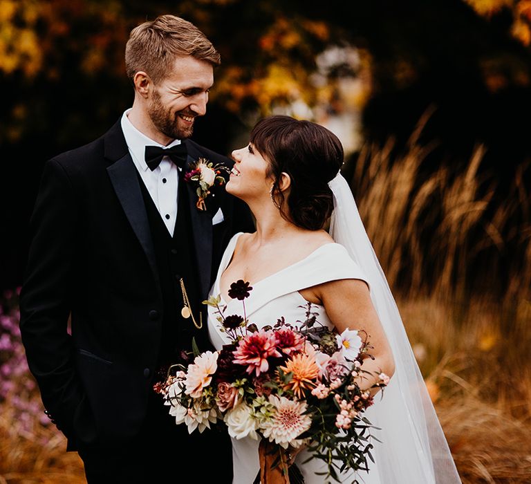 Autumnal rustic wedding with the bride in a bespoke off the shoulder v-neck wedding dress with the groom in a black tux with gold pocket watch 