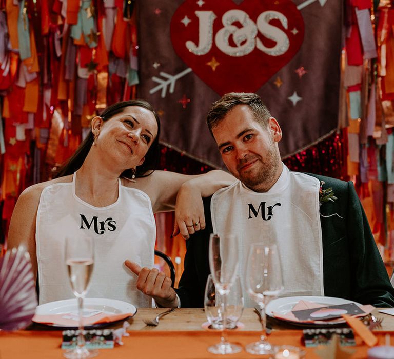 The bride and groom sitting at their wedding breakfast wearing mr and mrs bibs 