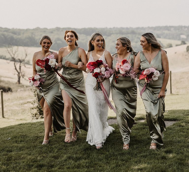 Bridal party photo with the bridesmaids wearing green satin bridesmaid dresses walking with the bride 