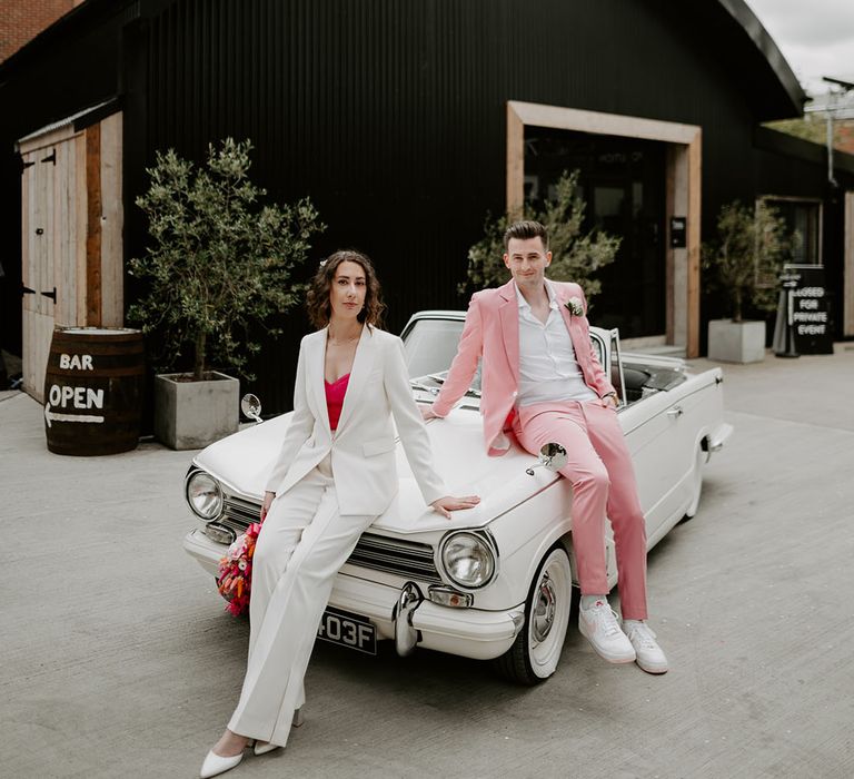 White retro wedding car for the disco 80s inspired wedding with the bride and groom posing together 