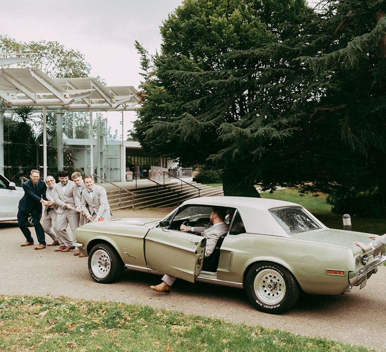 The groomsmen push the bride and groom in their green vintage Mustang wedding car 