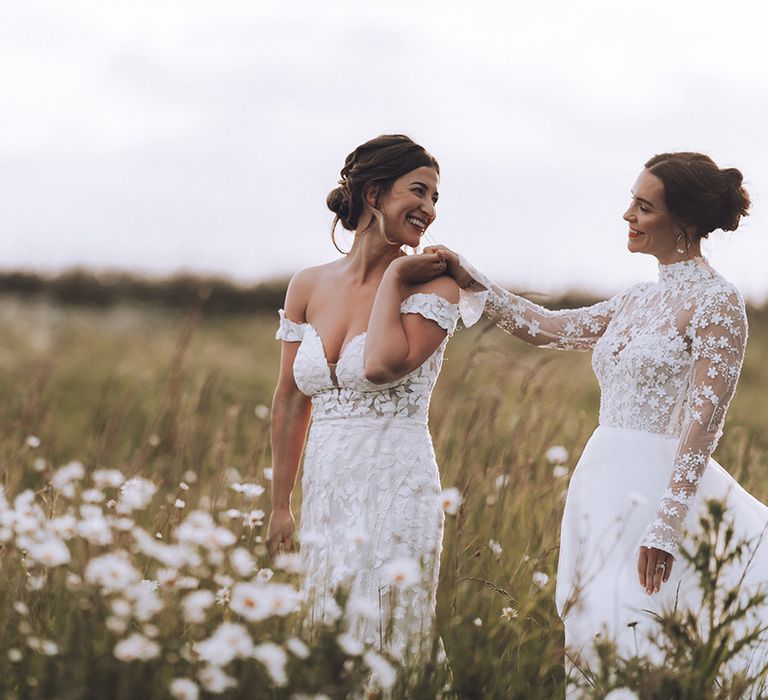 Two brides pose for their couple portraits in a field of daisies with flower wedding dresses 