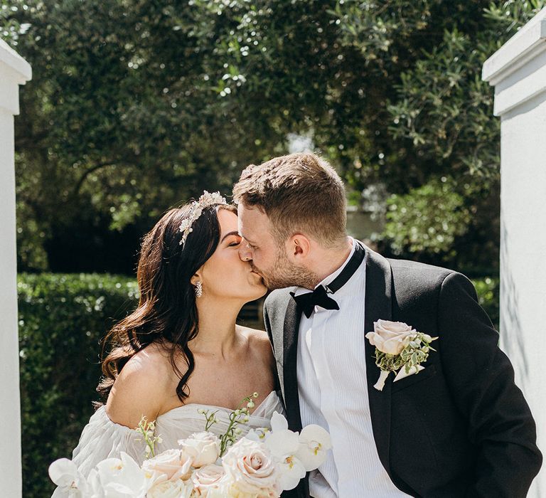 Bride in off the shoulder princess wedding dress carrying pink and white rose wedding bouquet with groom in black tuxedo 