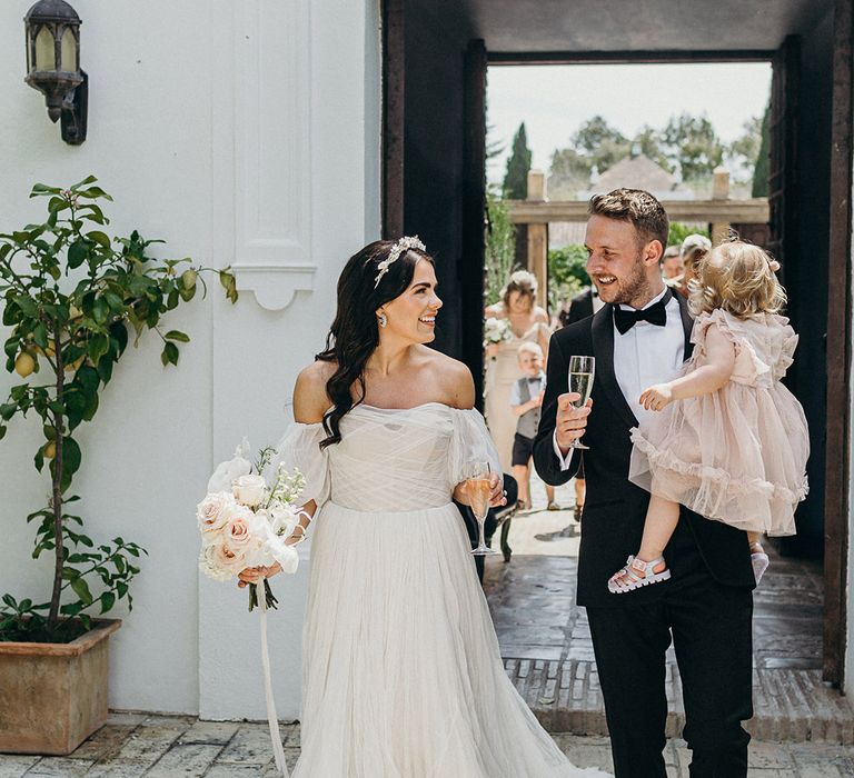 Bride carrying pink and white wedding bouquet with off the shoulder wedding dress walking hand in hand with groom in black tuxedo