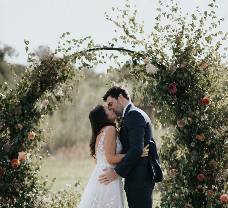 Bride and groom kissing in front of the ceremony floral moon gate at Willow Marsh Farm