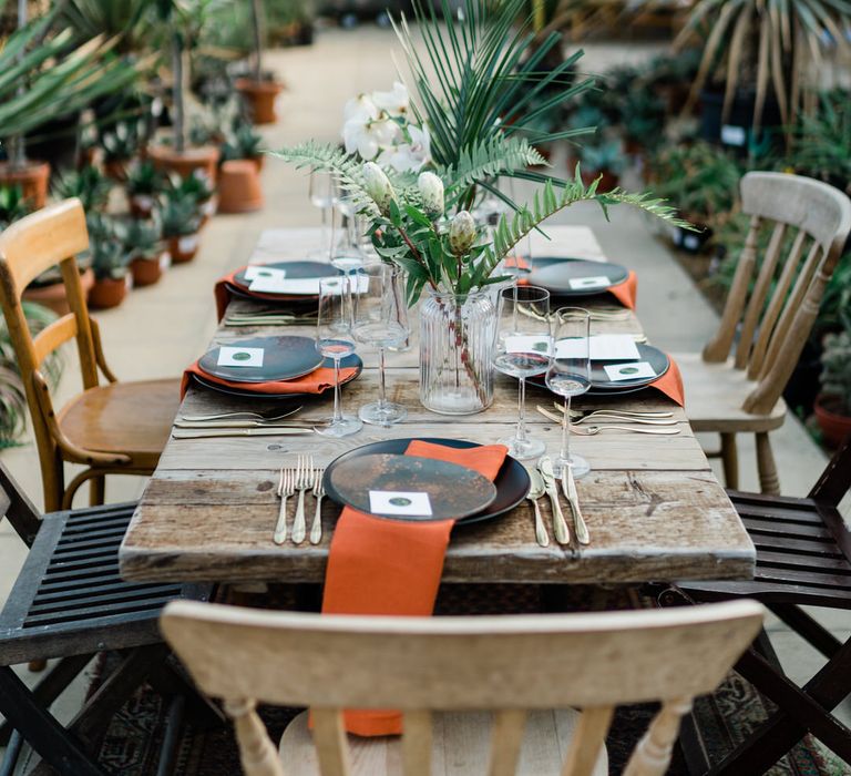 Rustic jungle wedding decor with orange napkins, jungle centrepiece and gold dinnerware