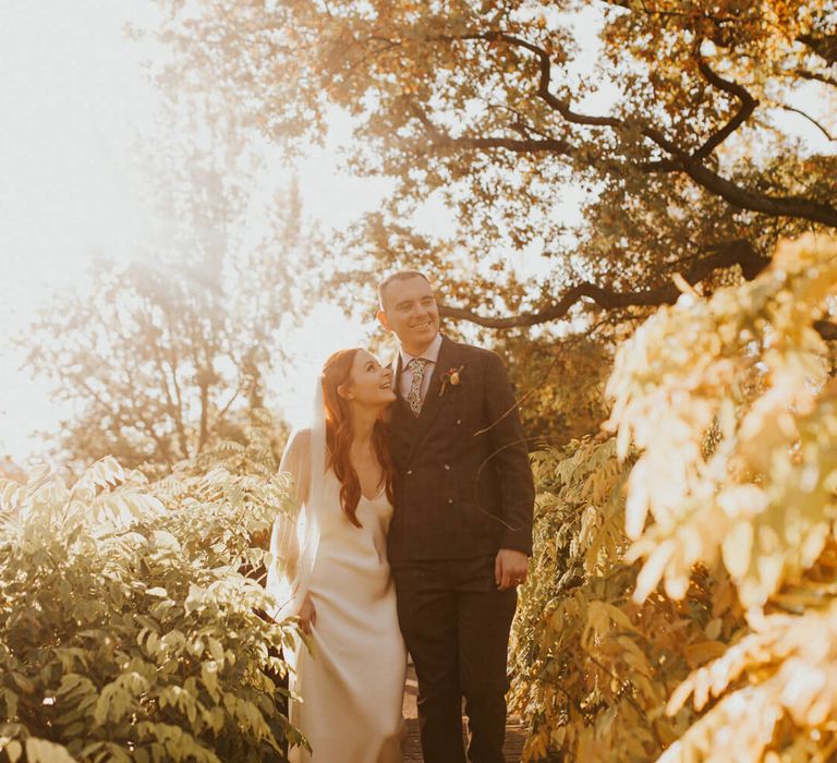 Newly married couple holding each other framed by autumnal leaves for outdoor wedding photography