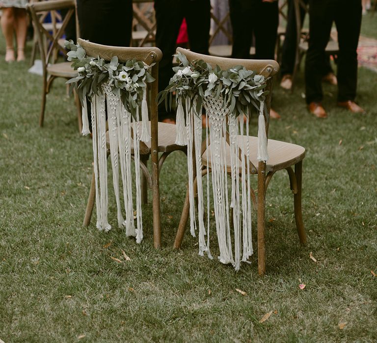 Macrame and foliage table back decor on wooden chairs for outdoor ceremony