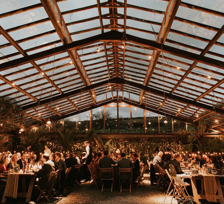 Glasshouse wedding reception decorated in fairy lights and candles 