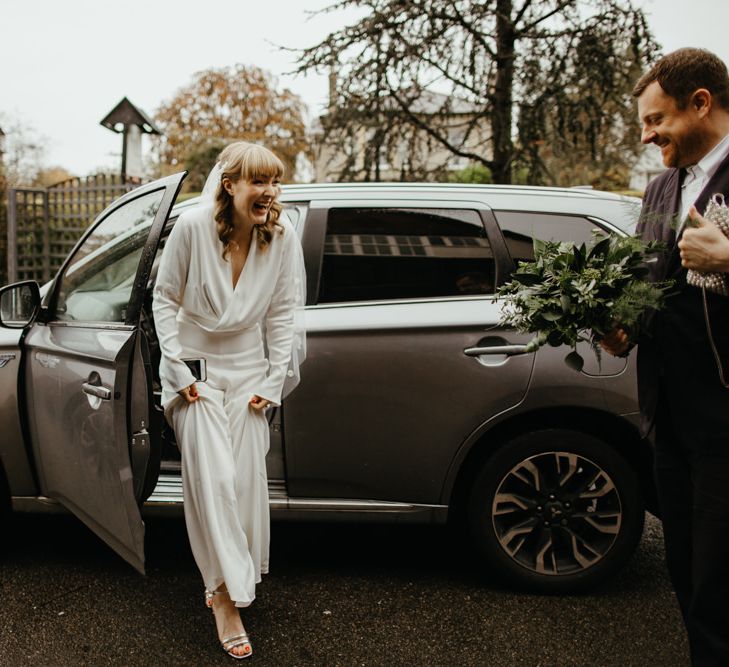 Smiley bride in a jumpsuit getting out of her wedding car 