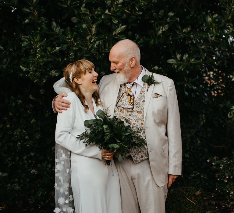 Father of the bride in a beige suit and floral waistcoat embracing his daughter 