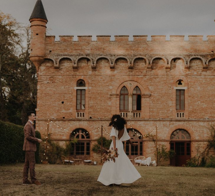 Groom in a brown wedding suit and bride in a low V back wedding dress with buttons dancing outside Château de Caumont wedding venue 