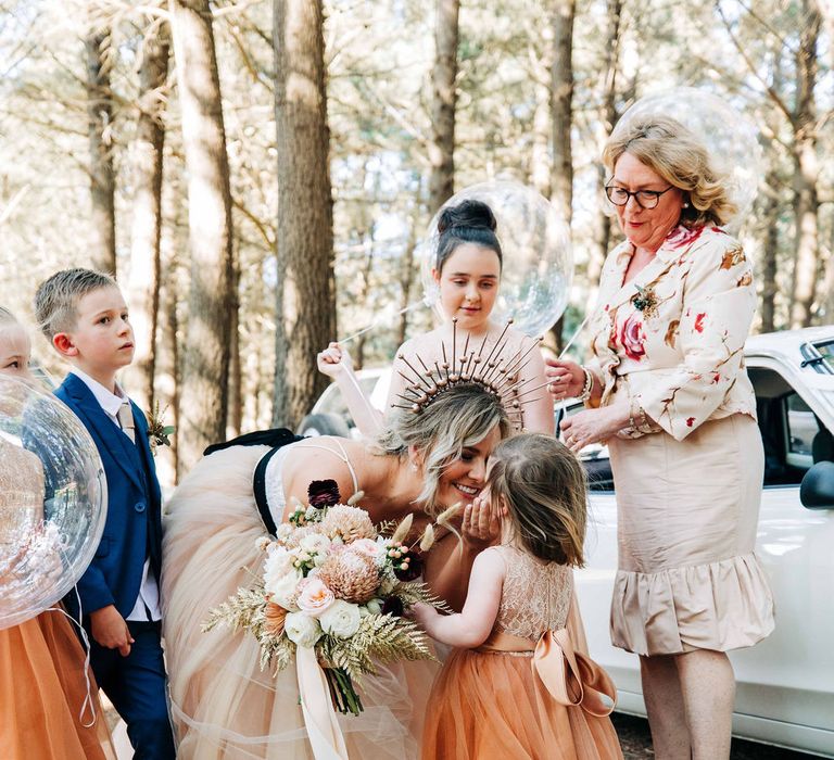 Bride in tulle wedding dress leans down to kiss flowergirl 