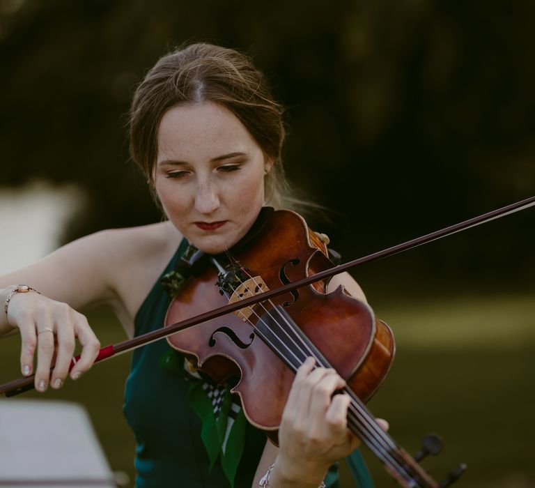 Woman in green silk dress plays viola at pink pampas grass wedding