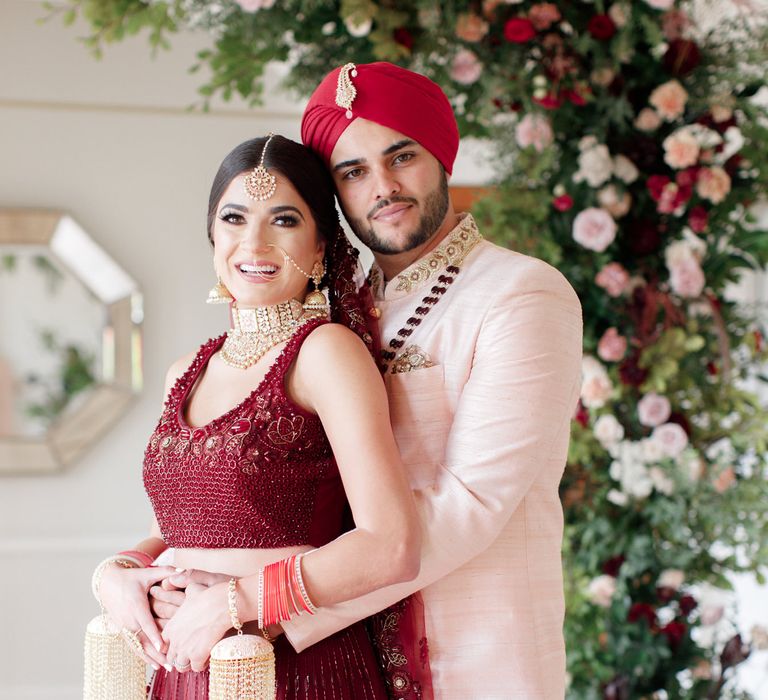 Sikh couple stand together in burgundy colour themed outfits