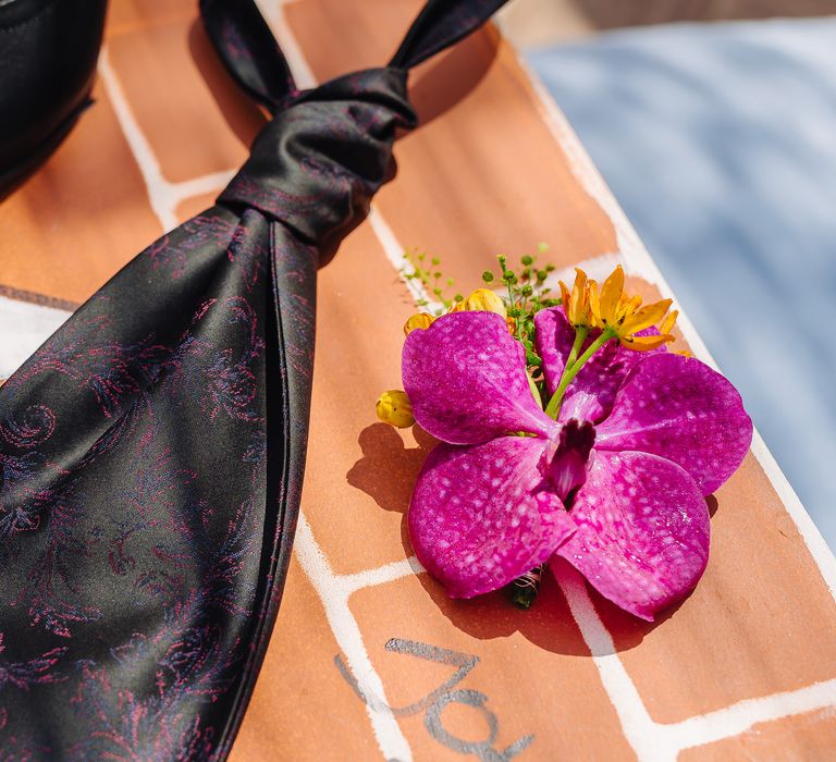 Black tie with colourful embroidery next to bright flower on brick wall