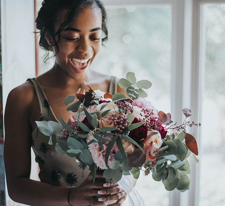 Bride on the wedding morning holding her red and green bouquet with eucalyptus, dahlias and roses