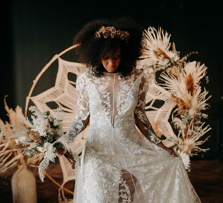 Bride lifts bridal gown skirt as she walks away from macrame backdrop