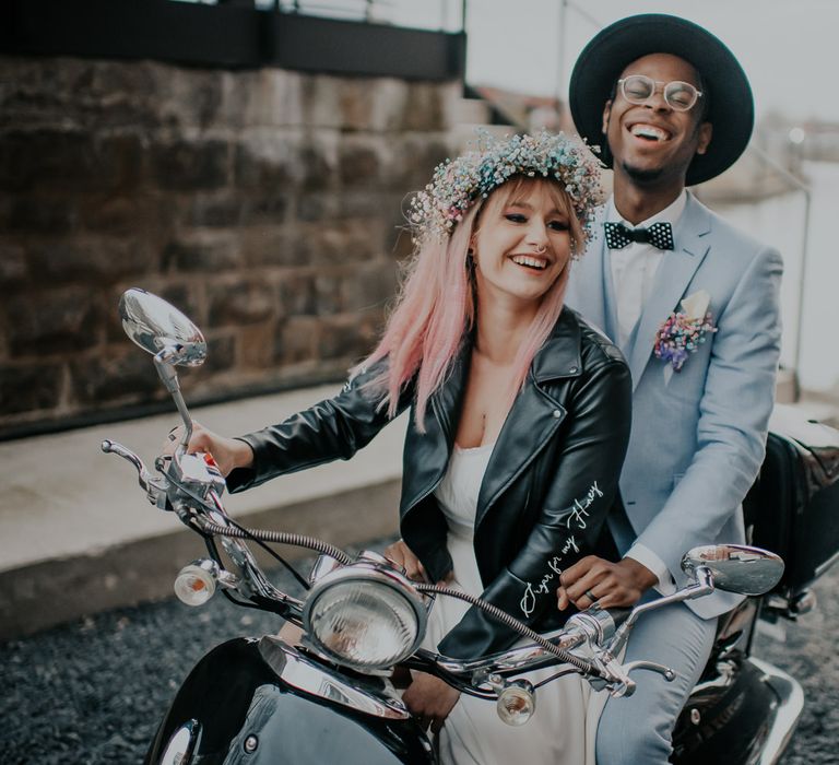 Bride and groom sitting on a motorbike in a leather jacket and flower crown and pastel blue suit and hat 