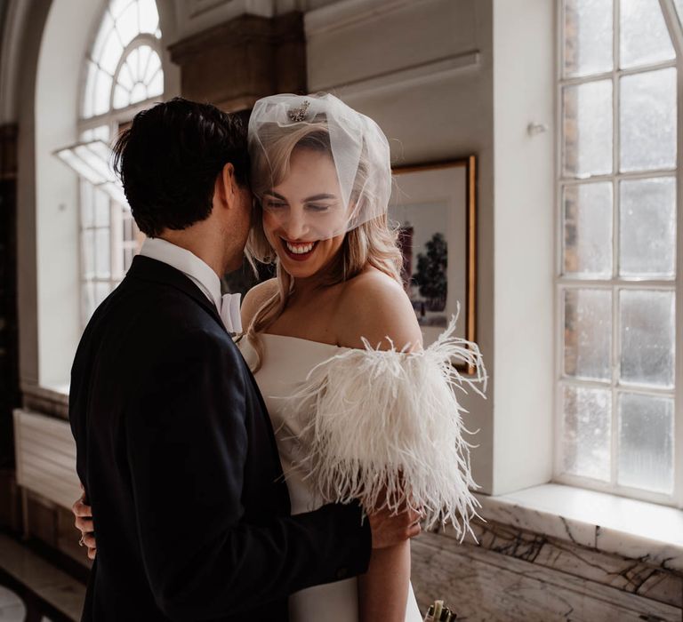 Groom holding his wife - bride wears off the shoulder wedding dress with feather detail 