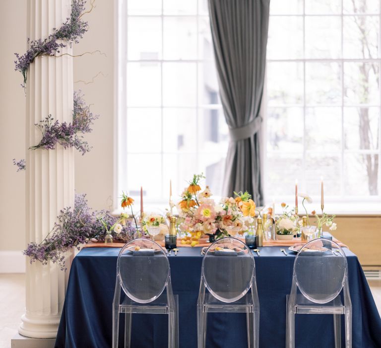 Art Nouveau table decor with blue tablecloth, perspex chairs, and pops of pastel floral displays 