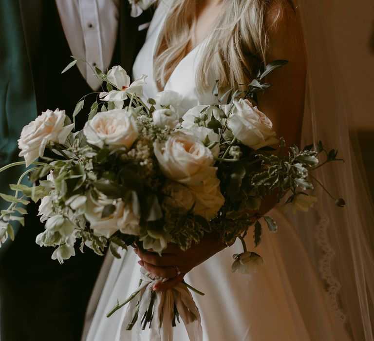 Bride looks down at floral bouquet whilst groom looks toward her 