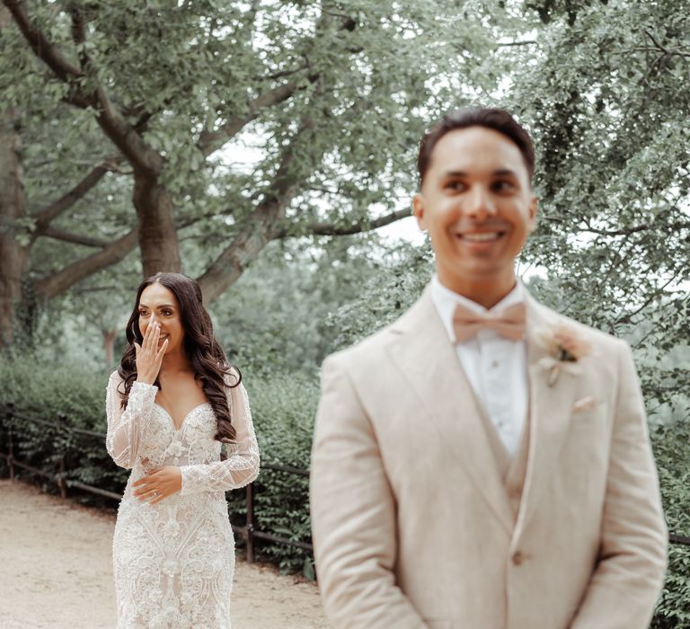 Groom awaits bride behind him as they move in for first look moment outdoors on their wedding day